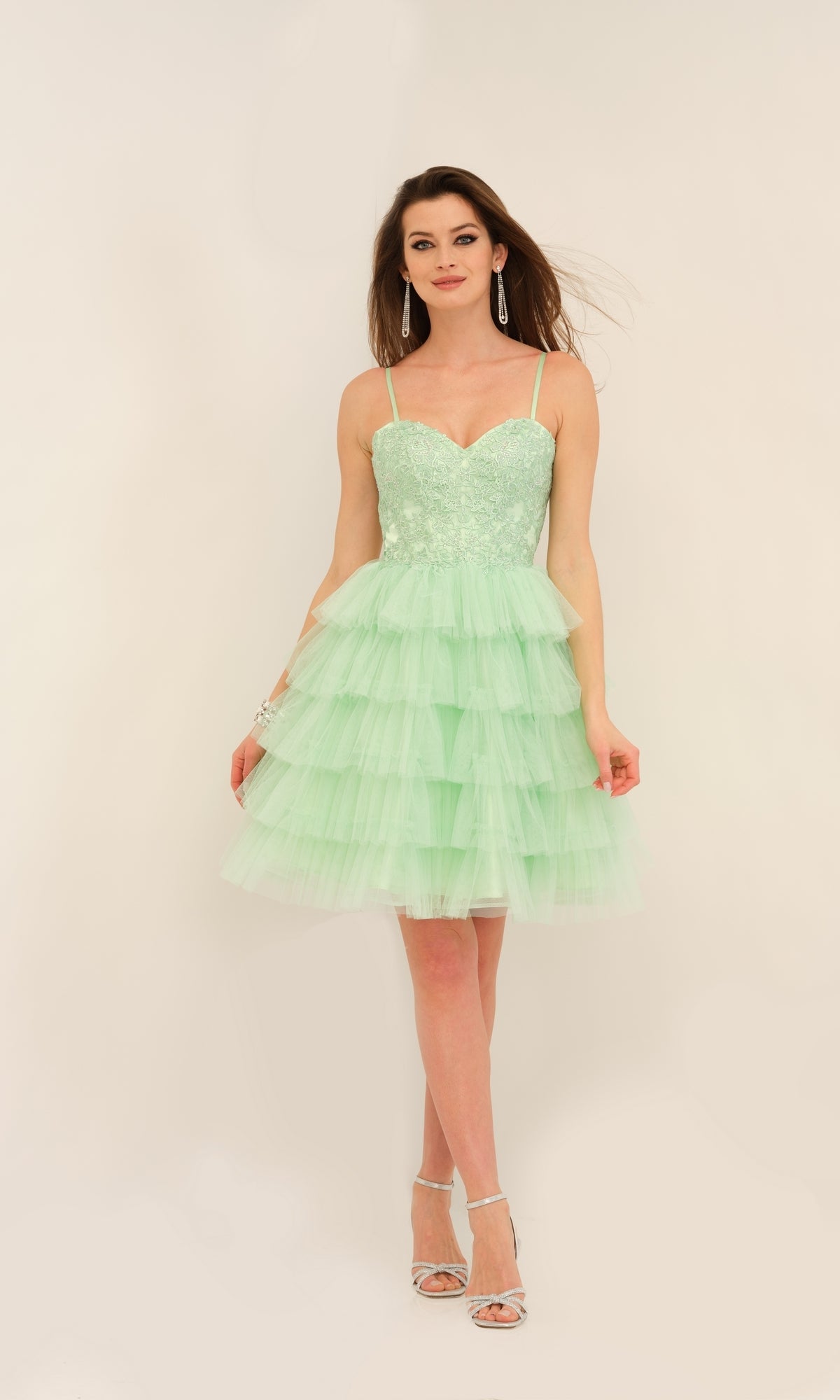 A woman poses in silver heels against a light background, wearing the Dave and Johnny Short Ruffled Hoco Dress 11182—a light green, sleeveless homecoming dress with an embroidered sweetheart bodice and flowing ruffled A-line skirt.